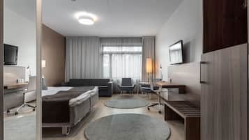 Une chambre d’hôtel moderne équipée d’un lit, de deux fauteuils, d’un bureau, d’une télévision et d’une grande fenêtre avec des rideaux.