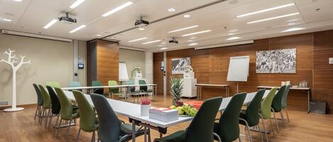 Un salón de conferencias con una larga mesa, sillas verdes, una pizarra y un proyector.