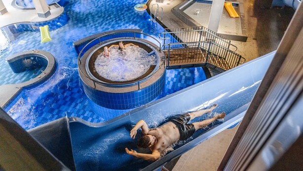 Tobogán de agua en una zona de piscina con jacuzzi y una escalera que lleva a un nivel superior.