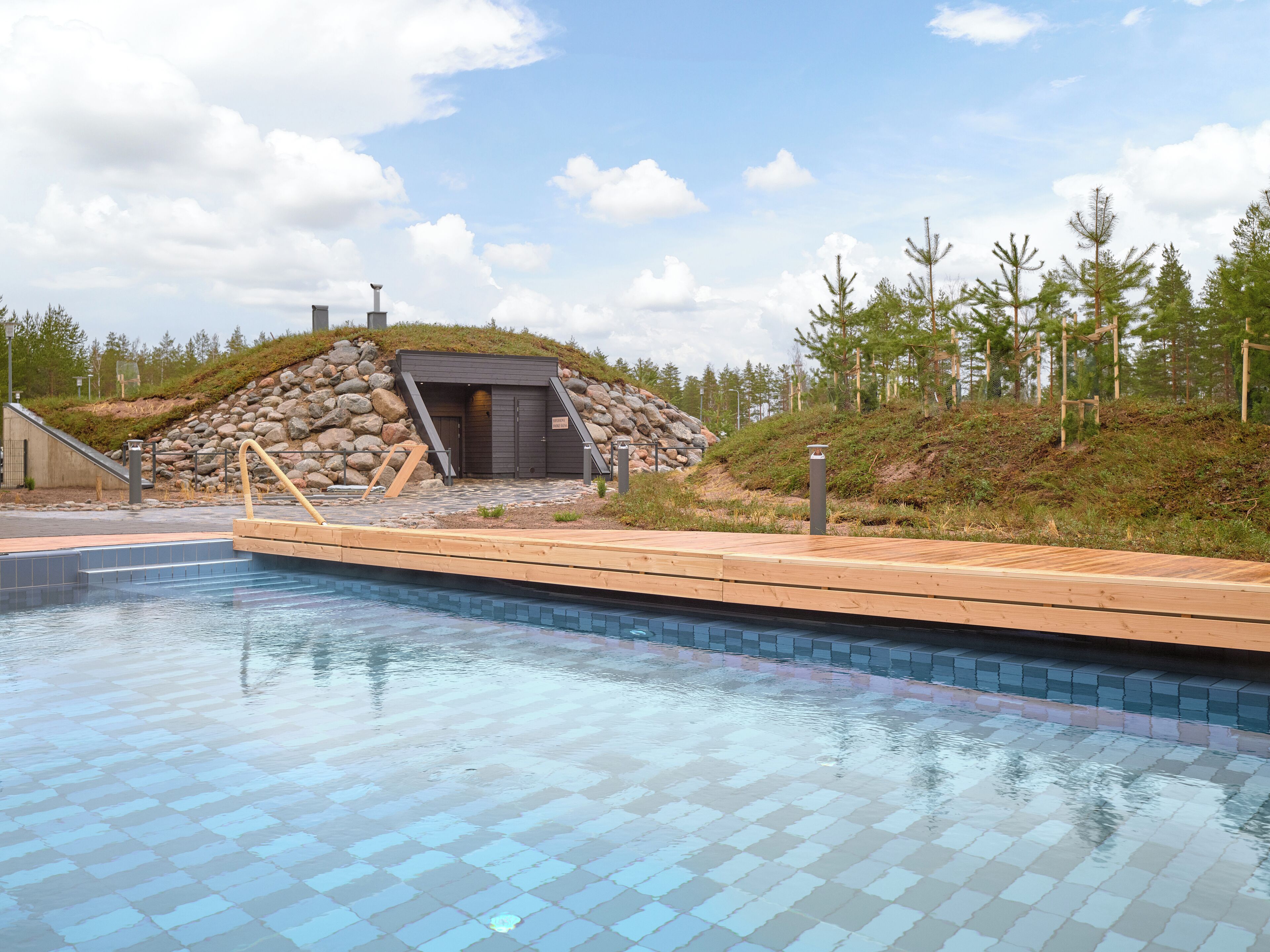Una piscina con muelle de madera y una estructura de piedra al fondo.