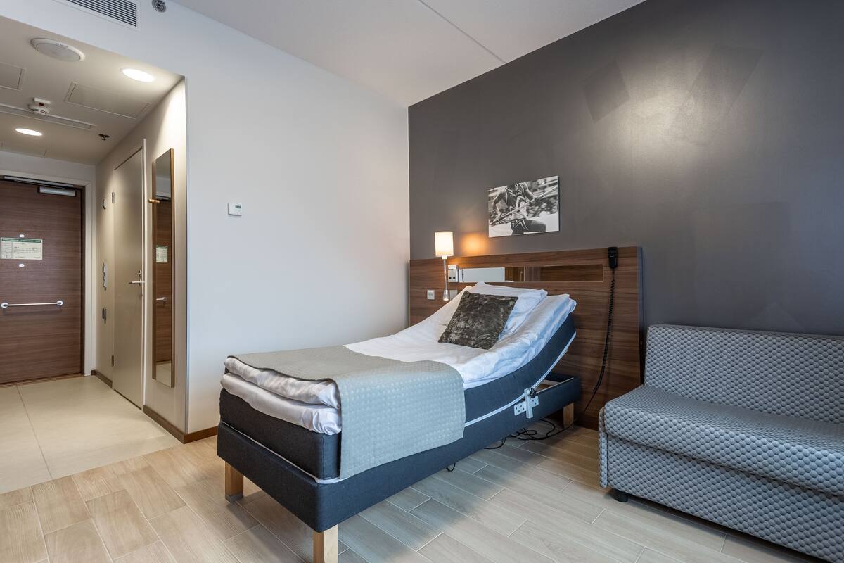 Ein modernes Hotelzimmer mit Bett, Nachttisch, Lampe und einer Couch.