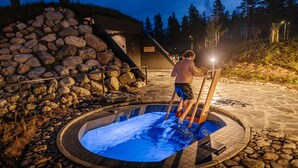 Una piscina de piedra con cubierta de madera, rodeada por un muro de piedra y una escalera de madera que sube.