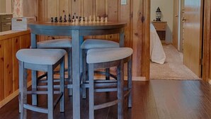 A wooden interior with a round table and four stools, a chandelier, and a hallway leading to another room. - Super Cute Cabin in the Pines (Lakeside)