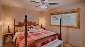 A bedroom with a four-poster bed, a ceiling fan, a window with a view of trees, and a bedside table with a lamp. - Super Cute Cabin in the Pines (Lakeside)