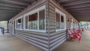 A log cabin with a covered porch, red chairs, and a view of the forest. - Super Cute Cabin in the Pines (Lakeside)