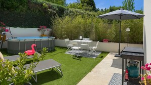 Un patio trasero con un jacuzzi, una mesa de comedor con sillas, una tumbona y una parrilla.