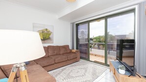 A modern living room with a brown sofa, a white floor lamp, and a large sliding glass door leading to a balcony.