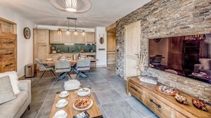 Ein modernes Wohnzimmer mit Steinwand, einem Essbereich mit Holztisch und einer Küche im Hintergrund.