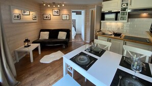 Un espacio habitable compacto con kitchenette, un sofá, una mesa de comedor para dos y una pequeña mesa blanca.