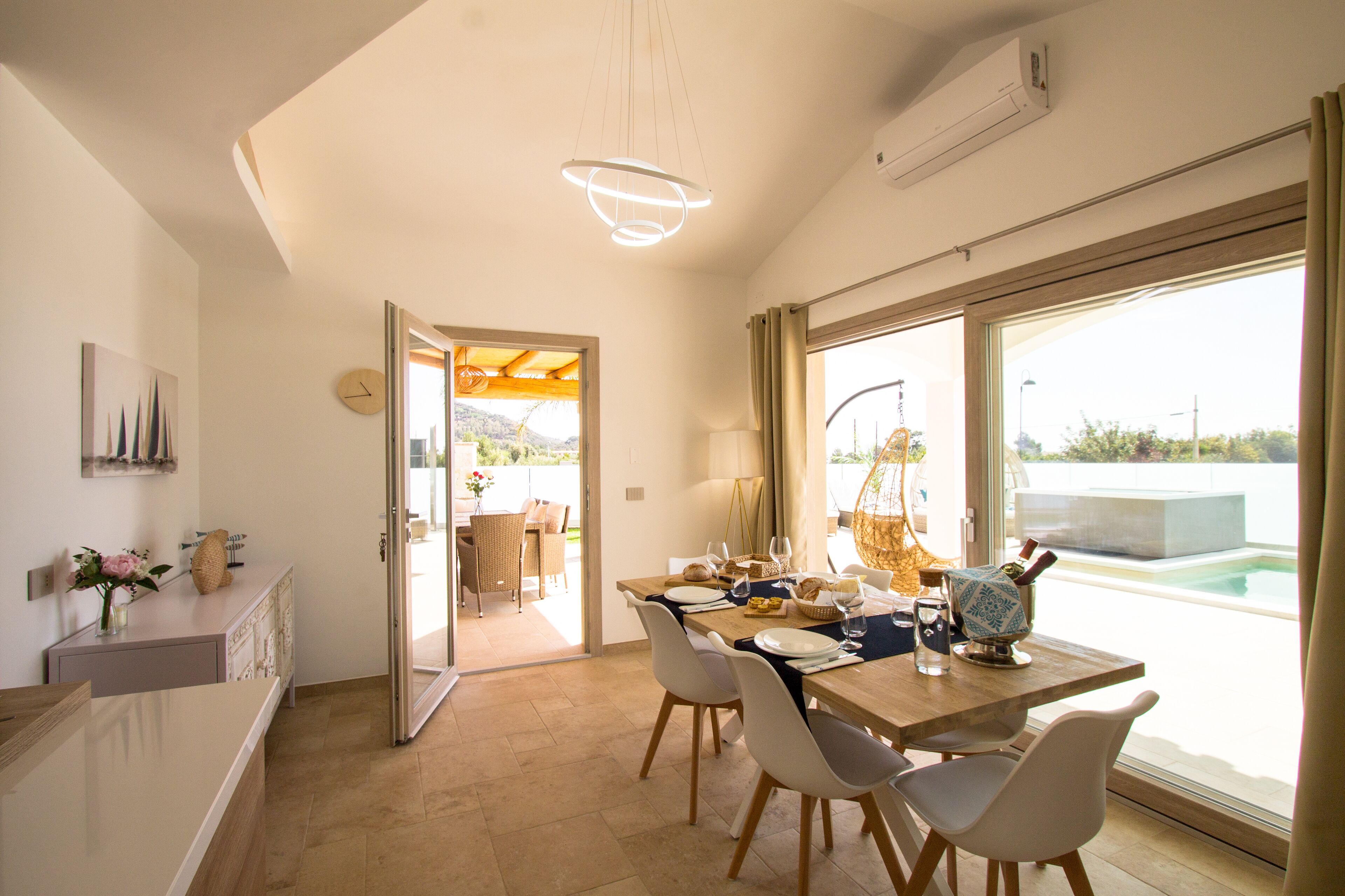 A modern dining area with a wooden table, white chairs, and a view of a swimming pool through large windows.