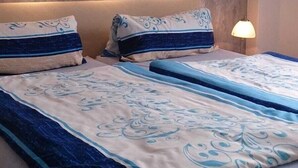 Ein Doppelbett mit blauer und weißer Bettdecke und passenden Kissen, eine strukturierte Wand im Hintergrund und eine Wandleuchte.