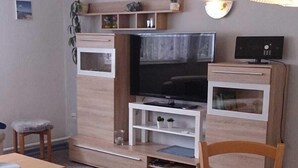 Ein kompakter Wohnraum mit Esstisch, Stühlen, einem Fernseher und einer kleinen Küchenzeile.
