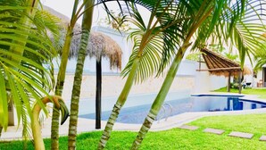 A pool area with a thatched roof structure, palm trees, and a bird. - Double Private Villa Playacar - Pool - Walk to Beach & 5th Avenue - Sleeps 22 (Playa del Carmen)