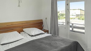 Een slaapkamer met een houten hoofdeinde, een bed met wit en grijs beddengoed, een bedlamp en uitzicht op buiten via een deur.