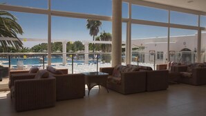 A spacious indoor area with large windows overlooking a pool and palm trees. There are several wicker sofas and a small table. - Cala Domingos Apartments (Manacor)