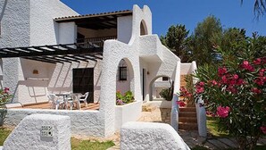 A white building with a patio area, outdoor seating, and a garden with pink flowers. - Cala Domingos Apartments (Manacor)