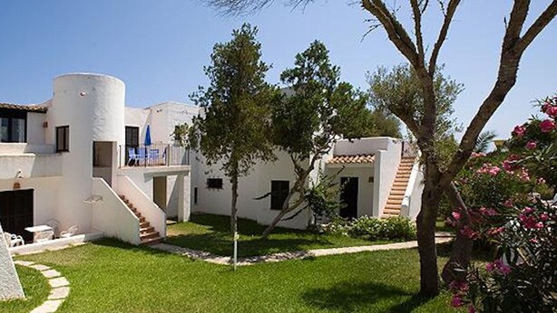 A modern building with a courtyard, featuring a staircase, a small pool, and a garden area with trees and flowers.