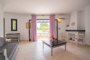 A room with a bed, a table, and a dining area with chairs. There is a window with curtains, a picture on the wall, and a fireplace. - Cala Domingos Apartments (Manacor)