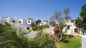 A row of white buildings with flat roofs, a paved pathway, and green landscaping. - Cala Domingos Apartments (Manacor)