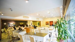 En rummelig restaurant med flere borde og stole, en disk og udsigt til det fri gennem store vinduer.