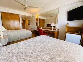 Habitación de hotel con dos camas, un escritorio, una silla, un televisor y un refrigerador pequeño.