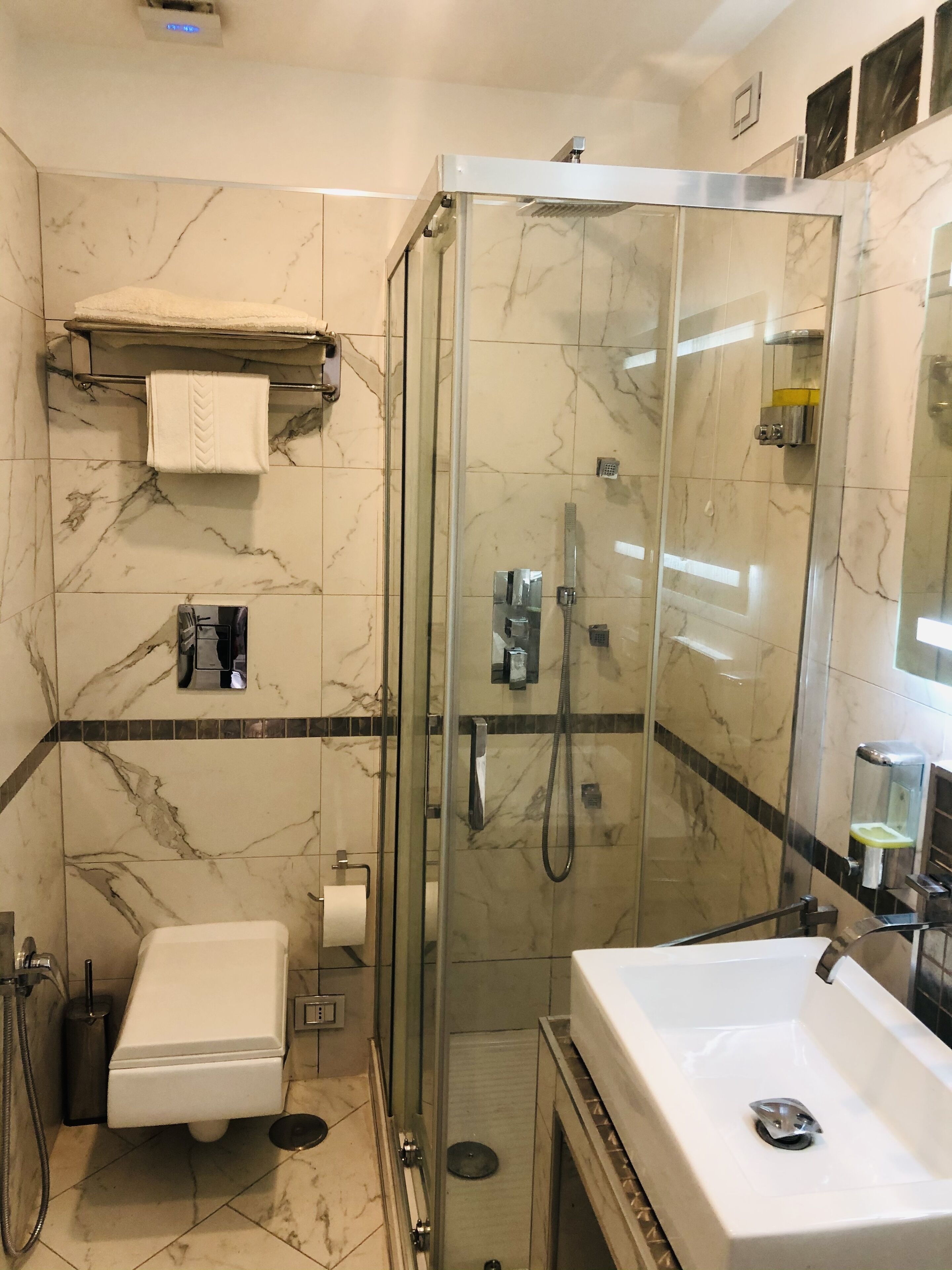 A modern bathroom with a glass-enclosed shower, a white sink, and marble-tiled walls.