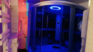 A modern, enclosed spa room with a control panel and a massage chair.