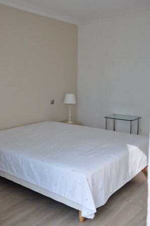 A bedroom with a bed, a nightstand, a lamp, and a small glass table.