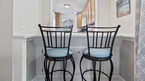 Una cocina con armarios de madera, encimera blanca y dos taburetes negros con cojines azules.