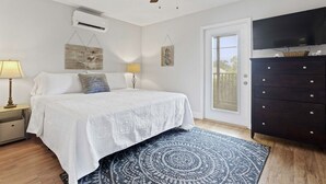 Un dormitorio con cama, ventilador de techo, aire acondicionado, cómoda, televisor y puerta con vista.