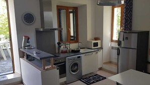 A compact kitchen with a washing machine, microwave, and a refrigerator. - Gîte de 4 Personnes Dans une Maison en Pierre de Pays (Matra)
