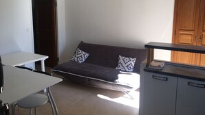 A compact living space with a sofa, a small table, and a kitchenette area. - Gîte de 4 Personnes Dans une Maison en Pierre de Pays (Matra)