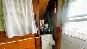 Une cuisine de taille réduite avec des murs en bois, un réfrigérateur blanc, une machine à café, un four à micro-ondes et un balai.
