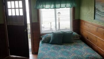 A room with a bed, a window with blinds, a door, and a ceiling fan.