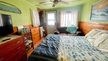 A bedroom with a bed, a television, a dresser, a ceiling fan, and a painting on the wall.