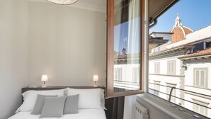 Una habitación de hotel con cama, dos lámparas de noche, ventana con vistas a edificios y un radiador.