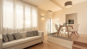 Una sala de estar moderna con un sofá, una mesa de comedor y sillas. Hay una zona de cocina con horno y refrigerador.