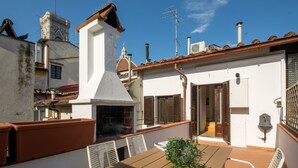 Una terraza en la azotea con mesa y sillas, una chimenea y vistas a edificios cercanos.