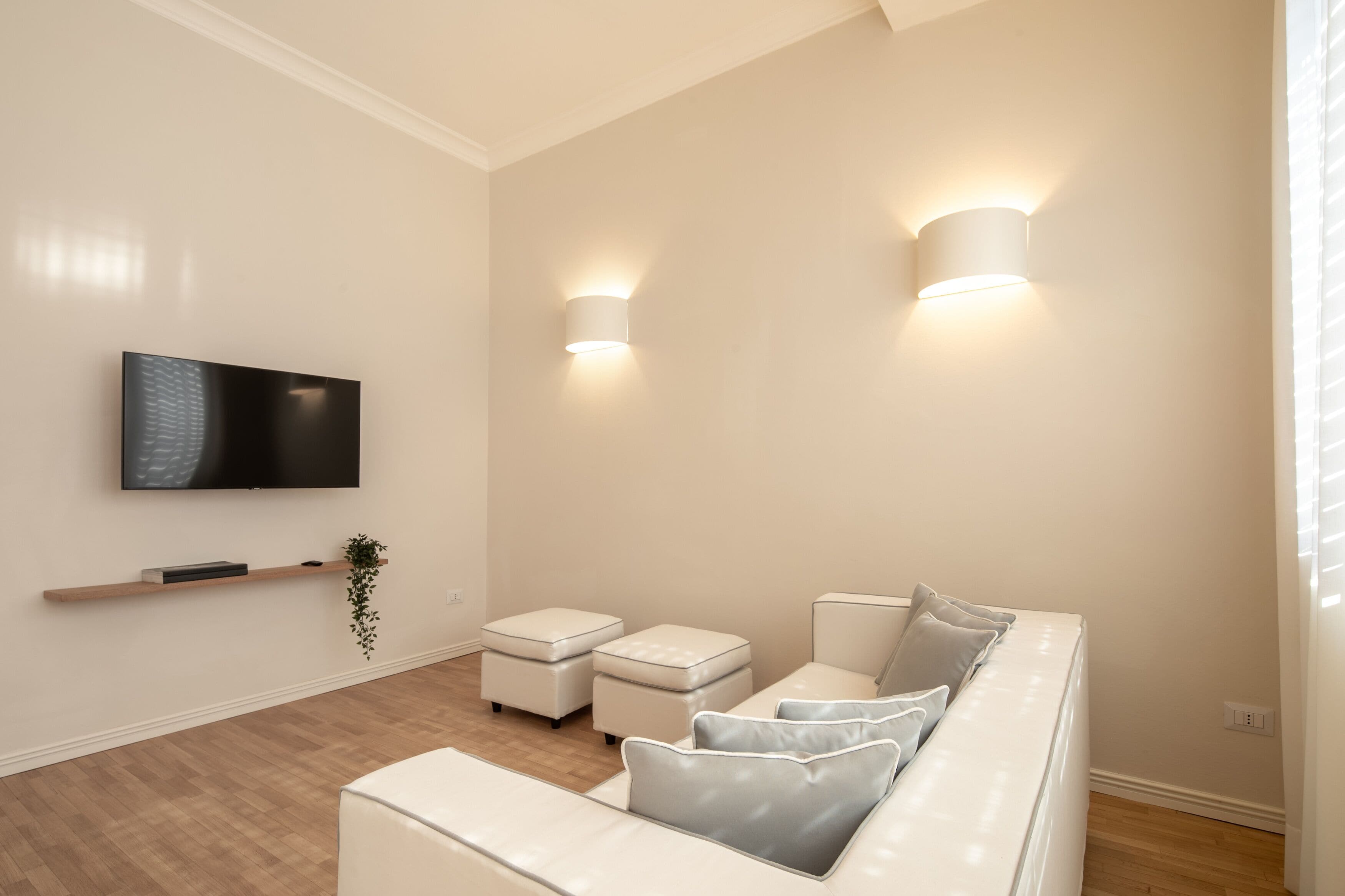 Een moderne woonkamer met een flatscreen televisie, twee wandlampen, een witte bank en een houten vloer.