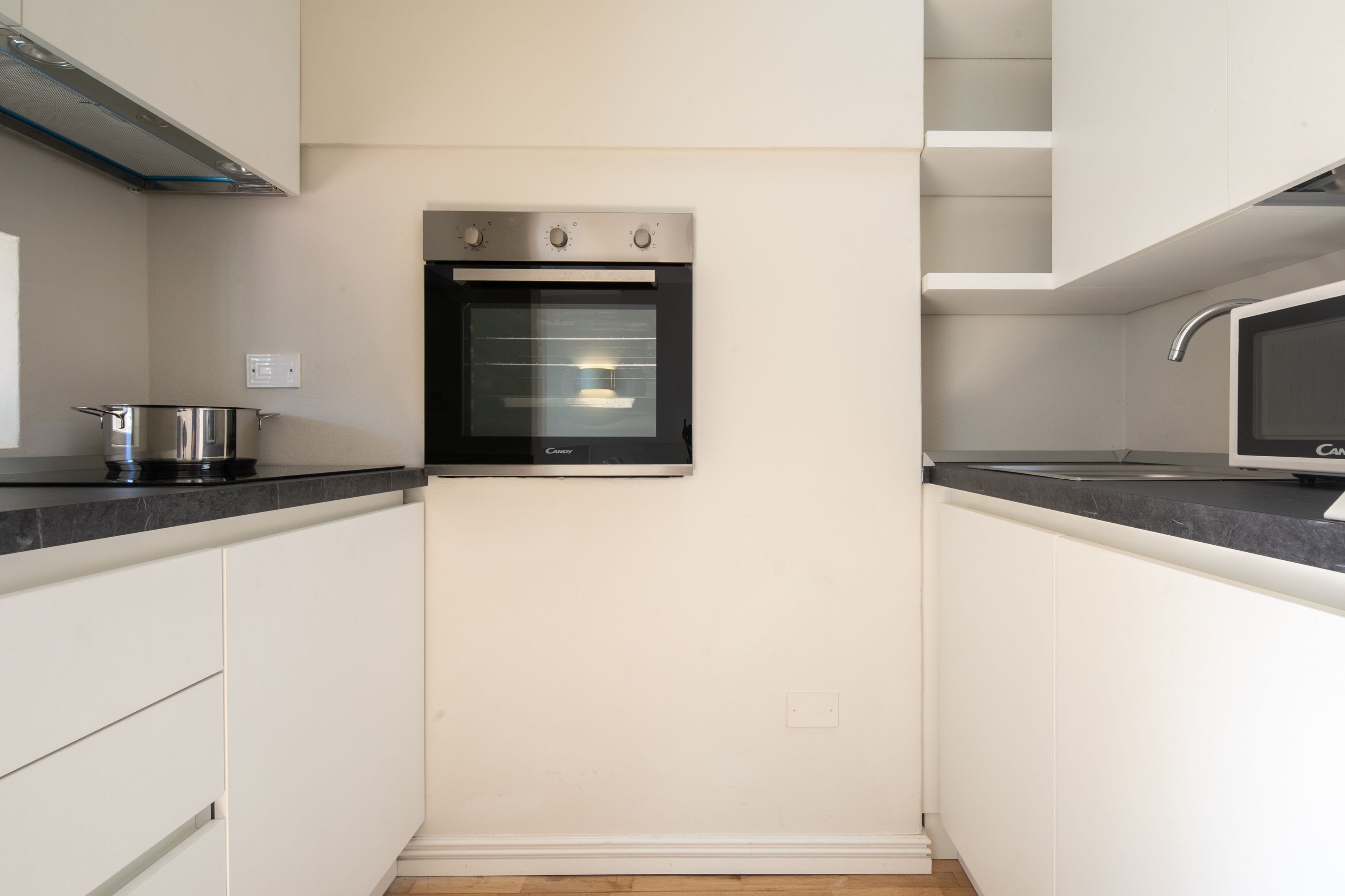 Una cocina moderna con armarios blancos, horno empotrado y campana extractora de acero inoxidable.