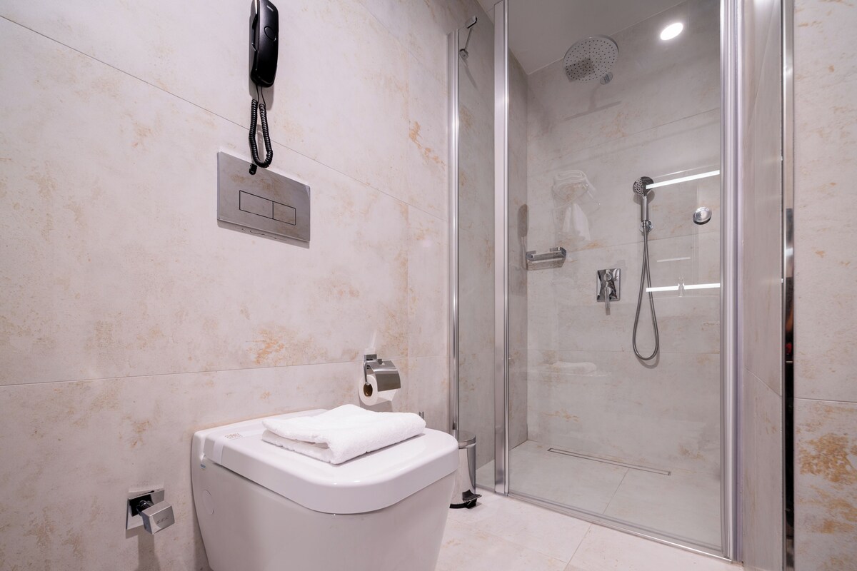 A modern bathroom with a toilet, a glass-enclosed shower, and a mounted telephone.