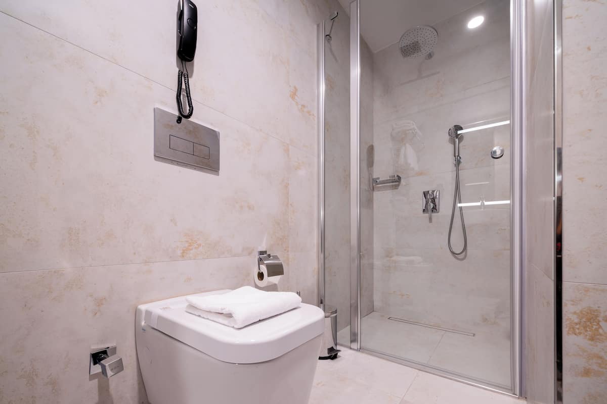 Un baño moderno con ducha envuelta en vidrio, un lavamanos blanco con una toalla y un teléfono instalado.