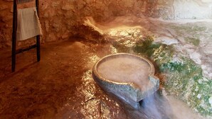 Interior de piedra en arco con una escalera de madera, un pequeño ventanal y una pila de piedra.