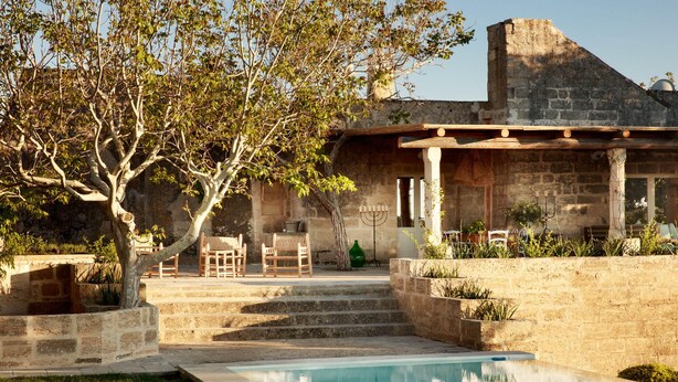 Un área de piscina con un muro de piedra, una pérgola y mobiliario exterior.