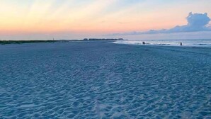 A beach with a wide sandy area and a calm sea. - Experience stunning oceanfront views at Nauti Time, a spacious 5-bedroom retreat in Holden Beach. (Holden Beach)