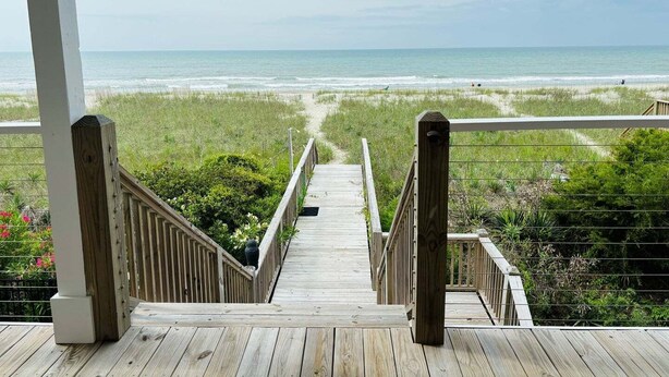 A wooden staircase leading to a beach view. - Experience stunning oceanfront views at Nauti Time, a spacious 5-bedroom retreat in Holden Beach. (Holden Beach)
