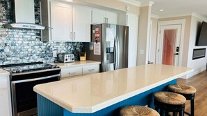 A kitchen with a central island, stainless steel appliances, and a blue accent wall. - Experience stunning oceanfront views at Nauti Time, a spacious 5-bedroom retreat in Holden Beach. (Holden Beach)