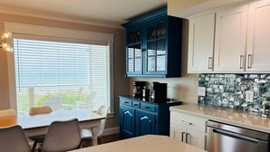 A kitchen with a dining table, chairs, a coffee maker, cabinets, and a dishwasher. - Experience stunning oceanfront views at Nauti Time, a spacious 5-bedroom retreat in Holden Beach. (Holden Beach)