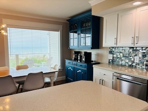 A kitchen with a dining table, chairs, a coffee maker, cabinets, and a dishwasher.