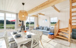 A spacious living area with a dining table set for four, a sofa with cushions, a staircase, and a large window offering a view of the outdoors. - Beautiful home in Zerpenschleuse with sauna (Zerpenschleuse)